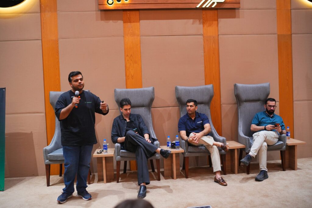 A moderator standing beside three seated panelists